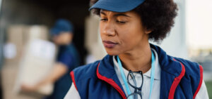 Logistics worker checking a package while a colleague loads boxes into a delivery van for third-party distribution.