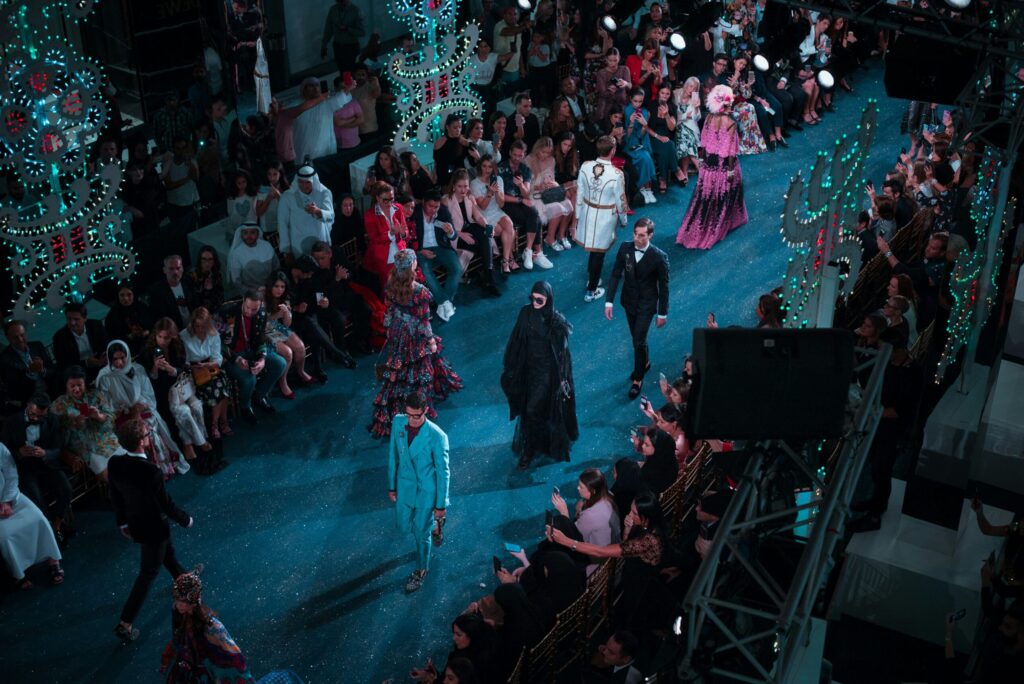 A runway show filled with models walking a brightly lit fashion catwalk surrounded by a large seated audience. The scene includes elaborate lighting, décor, and production elements, illustrating the type of high-pressure fashion events that rely on Mitchell’sNY Logistics for white glove delivery, event setup, delicate item handling, and time-sensitive transportation across the Northeast.