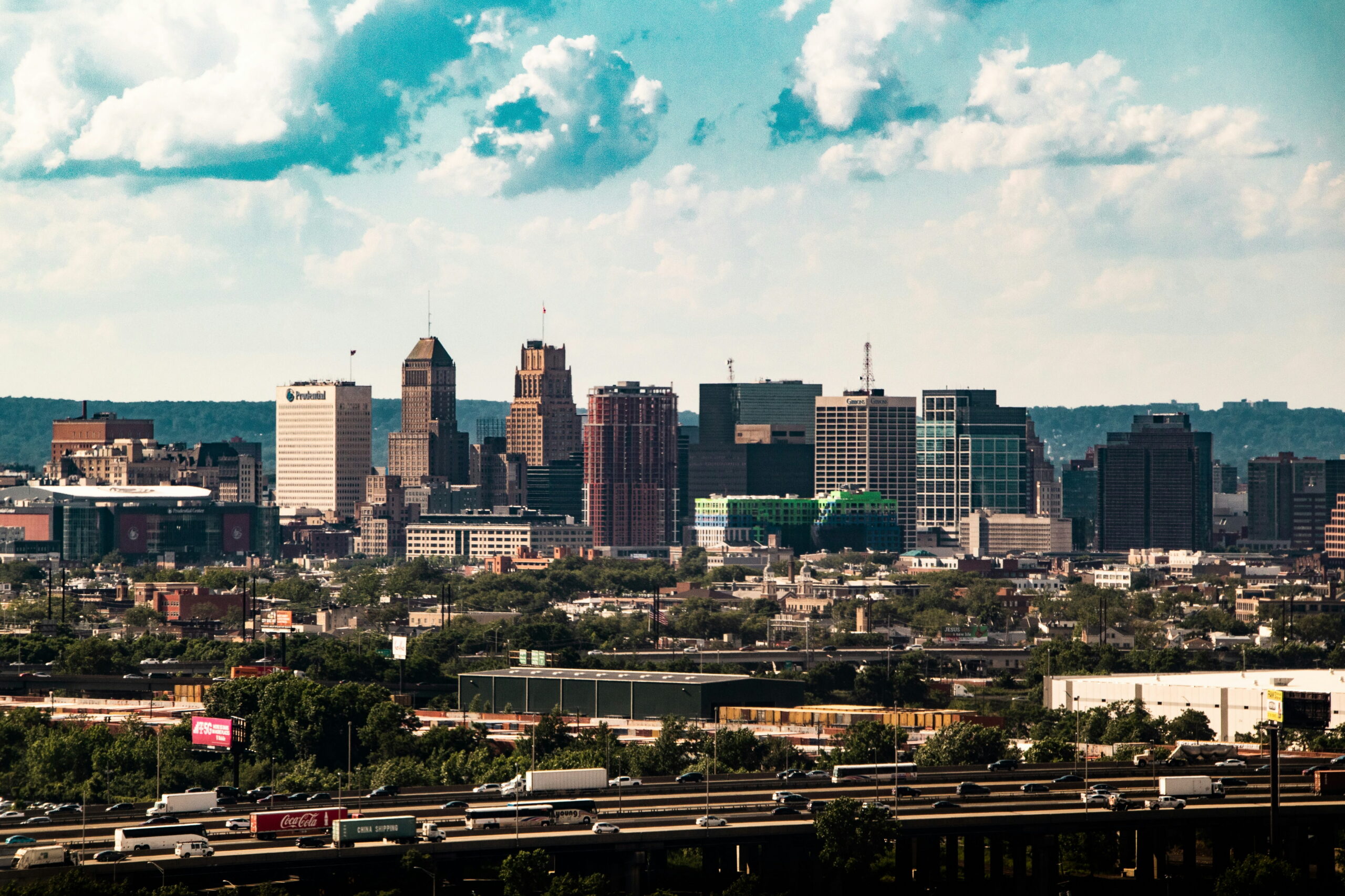 Wide view of the Newark, New Jersey skyline with downtown buildings rising above highways and industrial areas in the foreground.